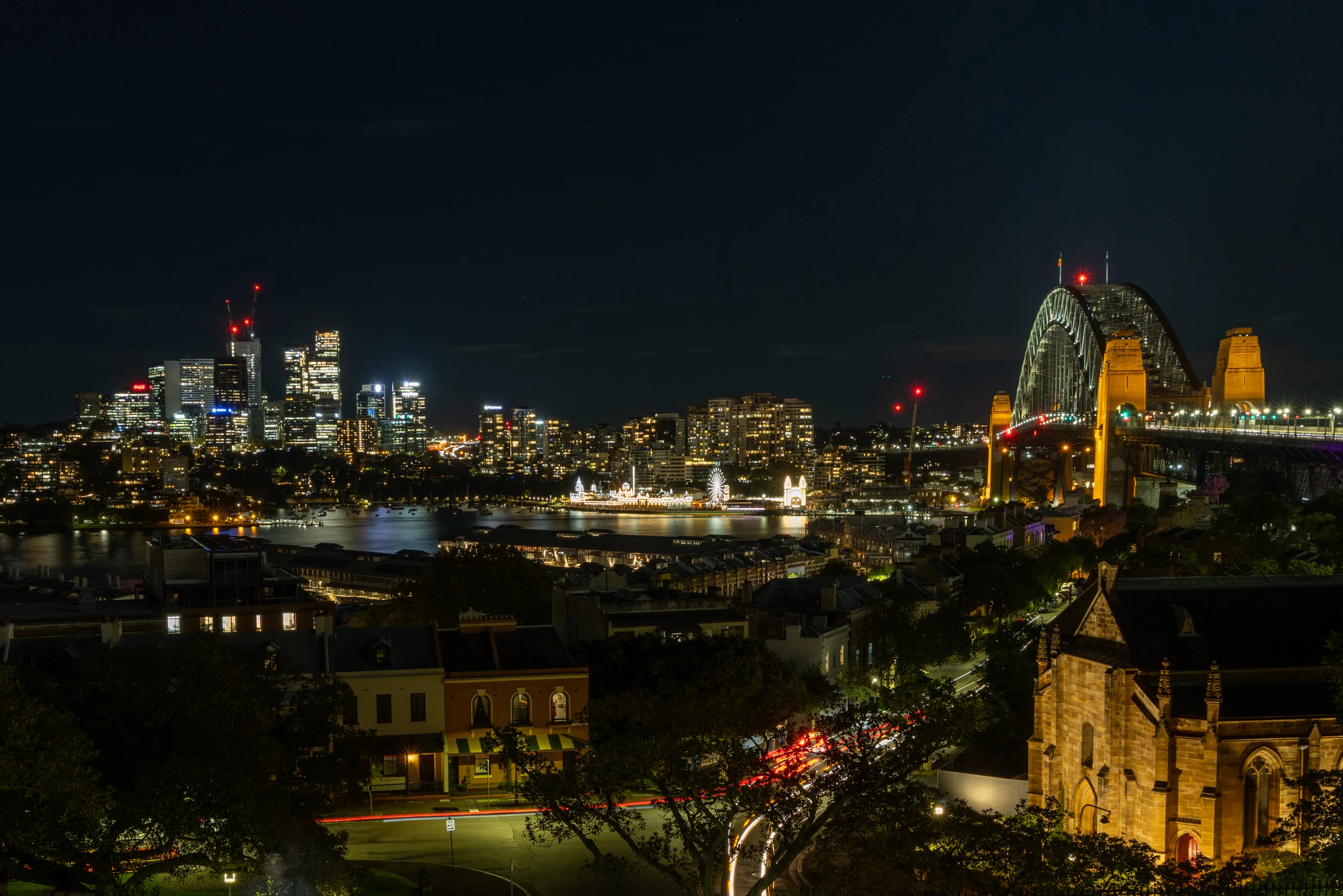 The view from the Observatory Hill rotunda at night, with Sydney Harbour, Sydney Harbour Bridge, Luna Park Sydney and tall buildings in the background